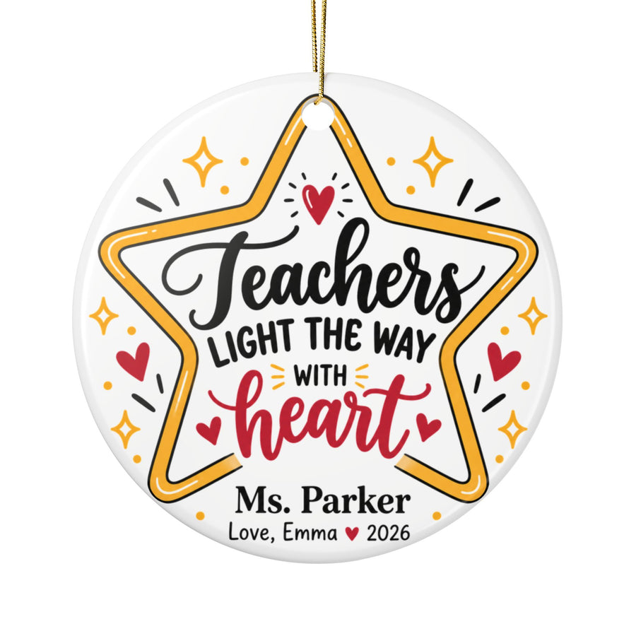 A round white ceramic Christmas ornament on a gold string, printed with "Teachers LIGHT THE WAY WITH heart" in black and red script inside a gold star outline with sparkles and hearts, with a sample teacher name and a "Love" signature with "2026".
