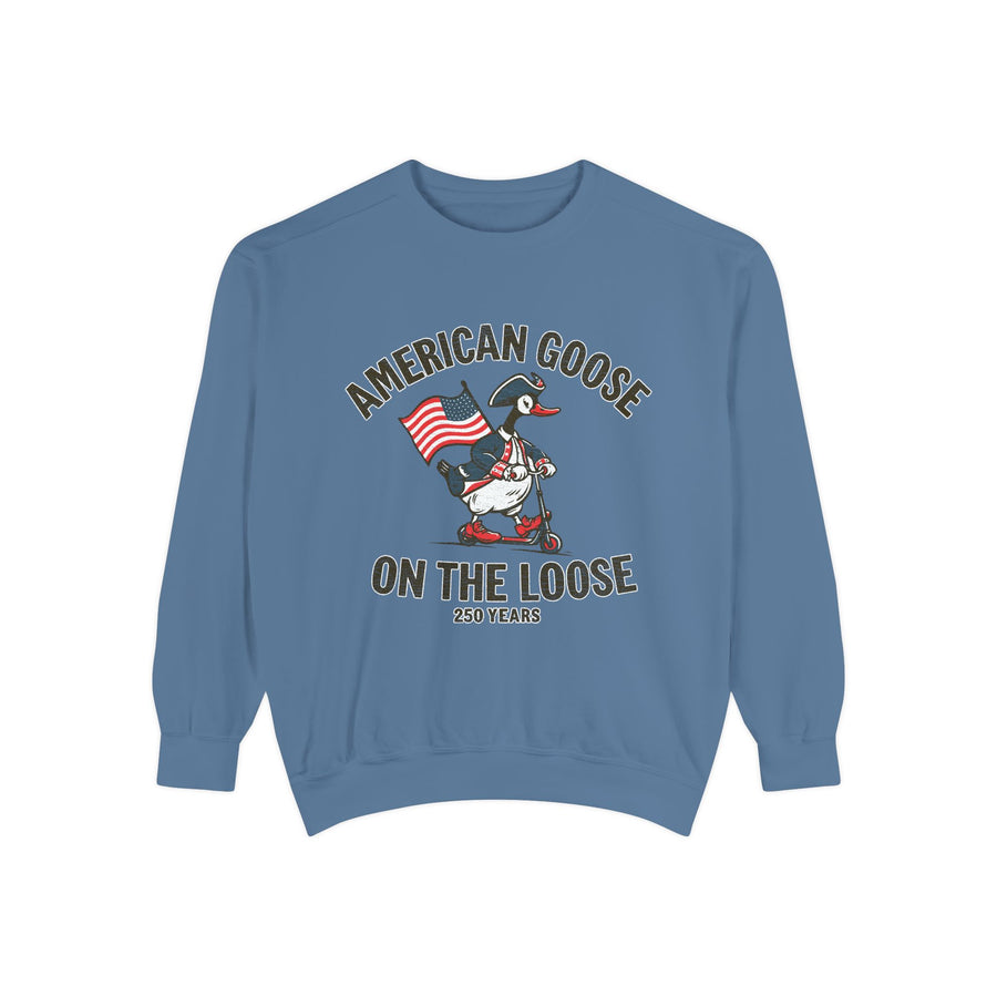A blue crewneck sweatshirt printed with a goose in a tricorn hat riding a scooter with an American flag between American Goose and On the Loose, 250 Years.