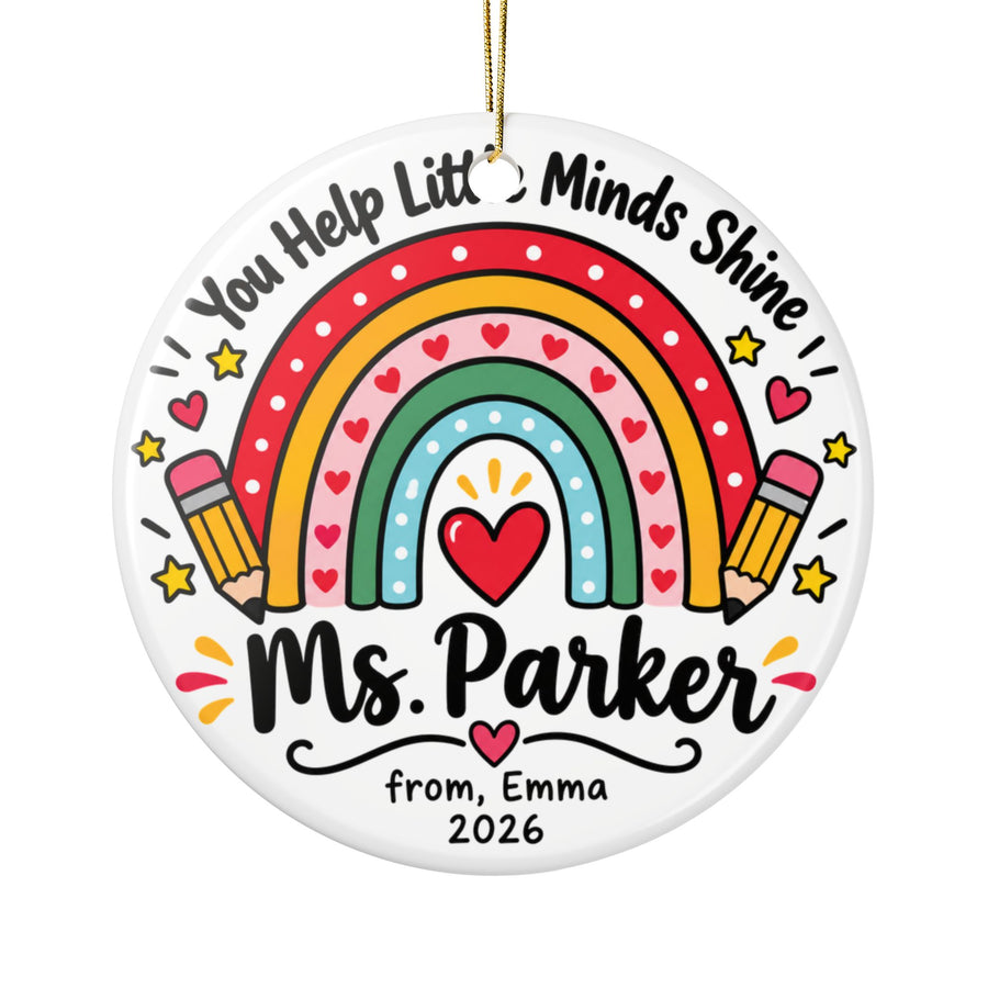 A round white ceramic Christmas ornament on a gold string, printed with a red, yellow, pink, green and blue rainbow with a red heart, two pencils and holly under arched "You Help Little Minds Shine" lettering, with a sample teacher name, a "from" signature and "2026".