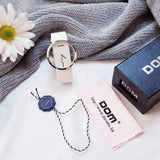 DOM white quartz watch styled as a flat lay with a daisy flower, gift box, and cleaning cloth