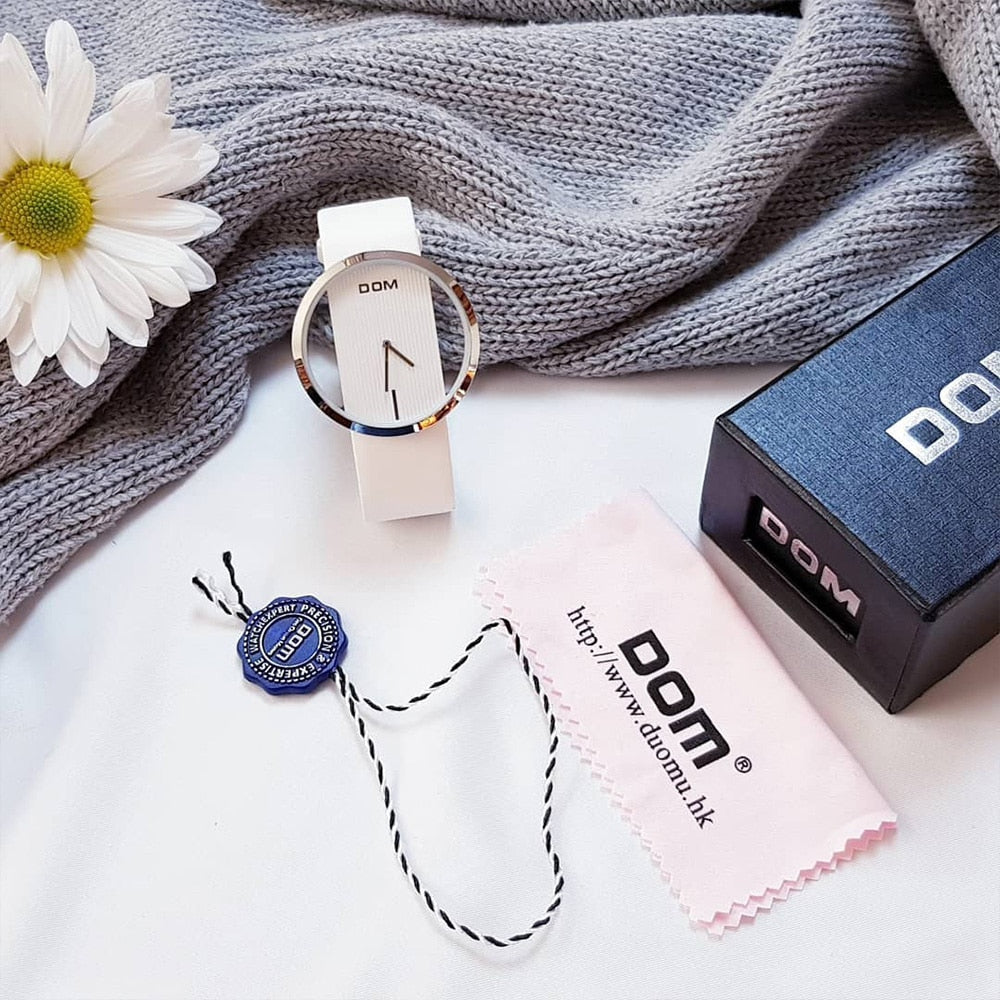 DOM white quartz watch styled as a flat lay with a daisy flower, gift box, and cleaning cloth
