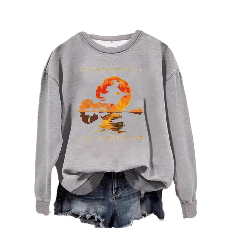 A gray crewneck sweatshirt printed with a witch flying across a large orange moon reflected in water.