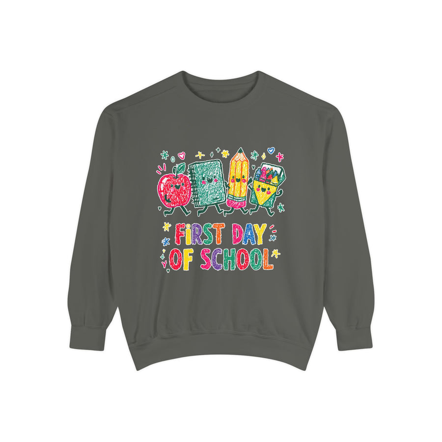 A dark gray crewneck sweatshirt printed with a cartoon apple, notebook, pencil and ruler above First Day of School in bright multicolored letters.