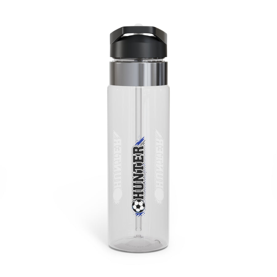 A clear Tritan water bottle with a black screw-on lid and straw, printed with soccer ball and player graphics and a name, styled with sports gear.
