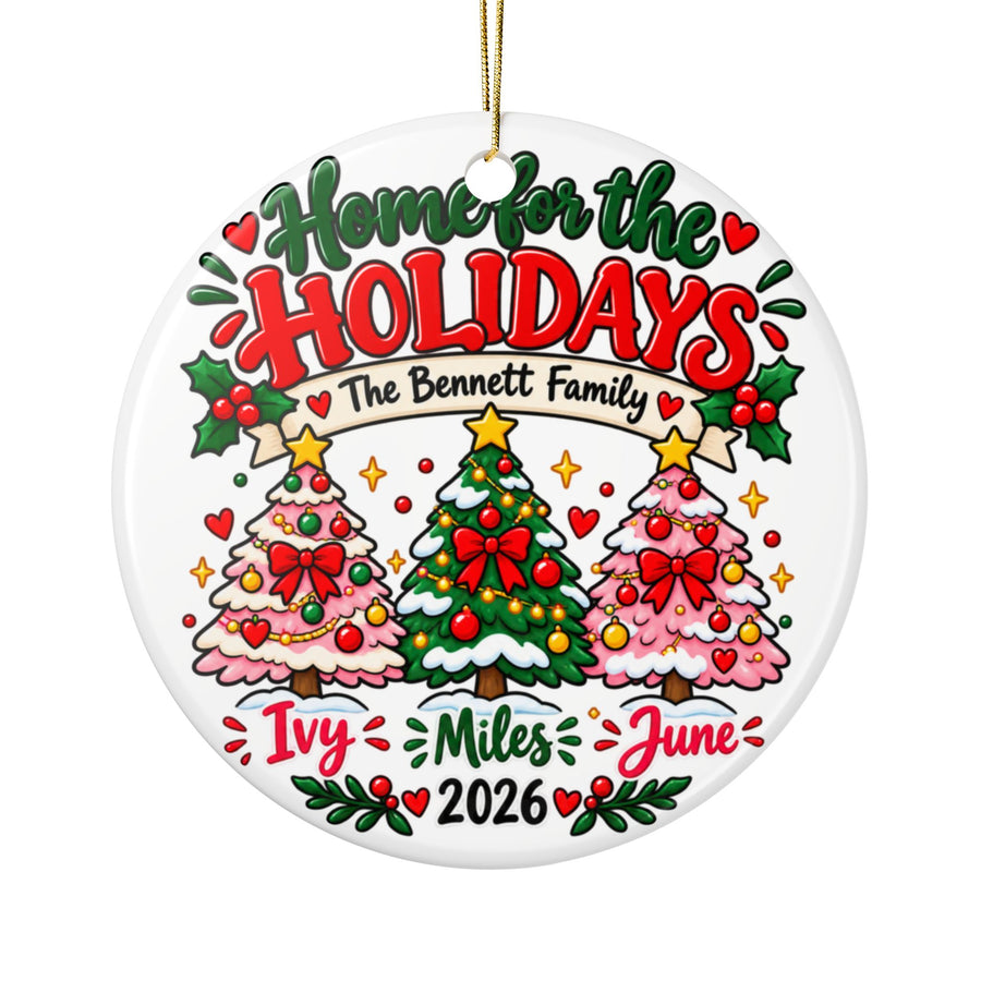 A round white ceramic Christmas ornament on a gold string, printed with "Home for the Holidays" in green and red lettering above a banner with a sample family name, three decorated trees in pink and green, three sample first names and "2026".