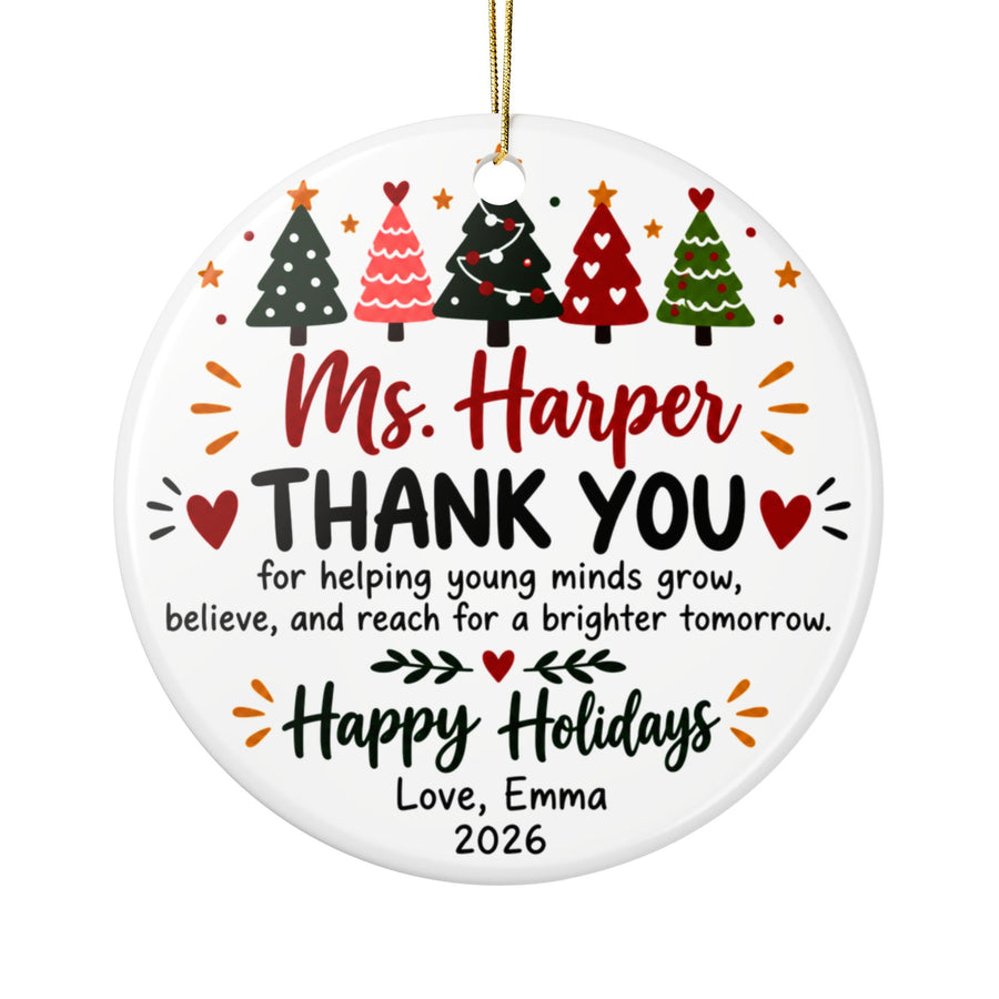 A round white ceramic Christmas ornament on a gold string, printed with a row of five decorated Christmas trees above a sample teacher name in red script, "THANK YOU for helping young minds grow, believe, and reach for a brighter tomorrow", "Happy Holidays" and a "Love" signature with "2026".