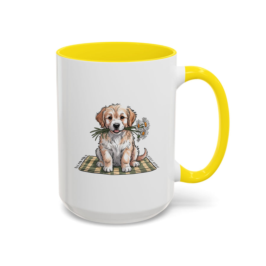 A white ceramic mug with a colored handle and interior, printed with a fluffy cream and tan puppy holding white daisies in its mouth, sitting on a green gingham blanket.