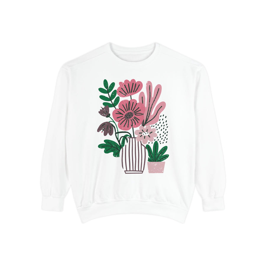 A white crewneck sweatshirt printed with pink and purple flowers in a striped vase beside a small potted plant.