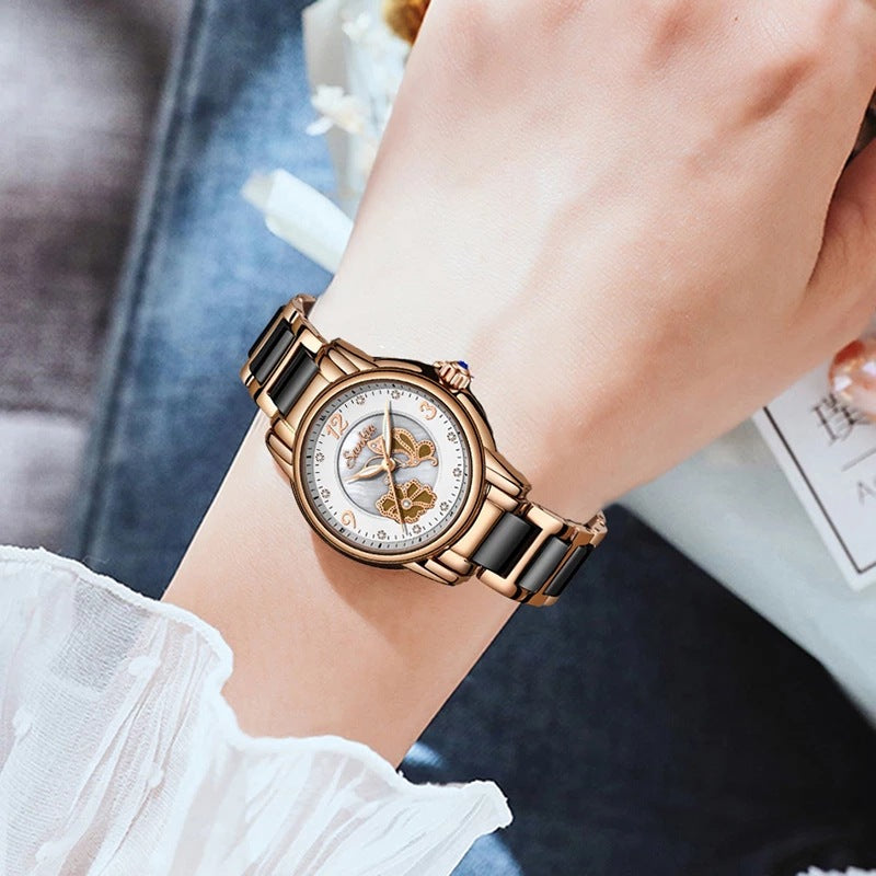 A rose gold and black ceramic link watch shown twice, once close up and once worn on a wrist, its pale dial set with two butterflies and a ring of small clear stones around the outer edge of the dial.