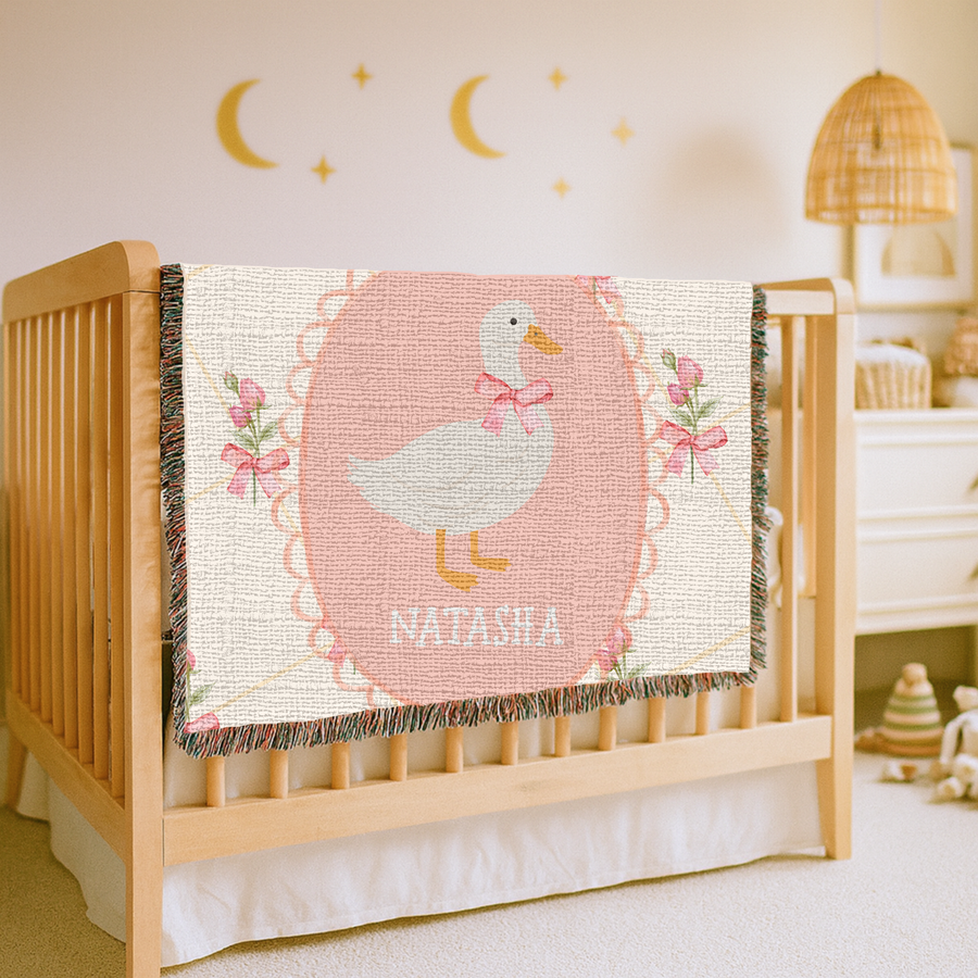 Cream fringed woven blanket with a gold lattice and pink roses and bows, centred on a scalloped pink oval holding a white goose in a pink neck bow above the name Natasha.
