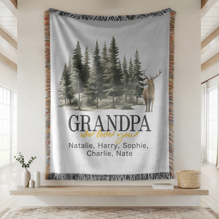 White fringed woven blanket printed with a watercolour pine forest and a standing antlered stag, reading Grandpa above we love you in gold and five names in a line beneath.