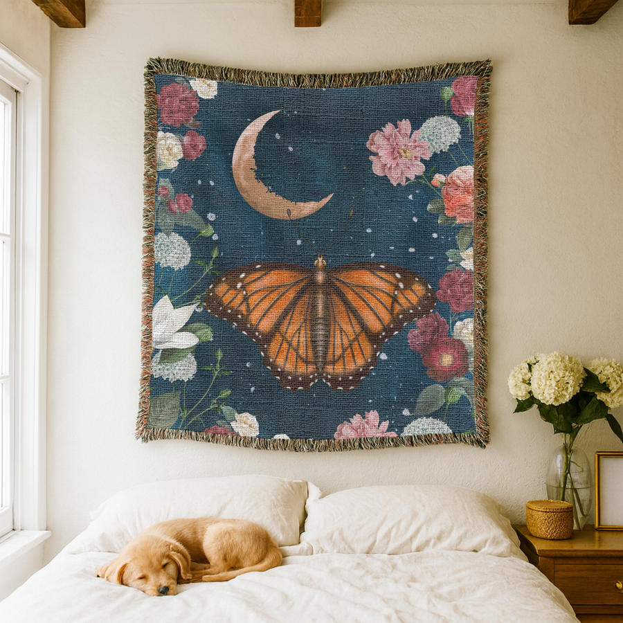 Deep blue fringed woven blanket printed with a large orange butterfly at its centre beneath a crescent moon, ringed with roses, peonies, magnolia and white hydrangea heads.