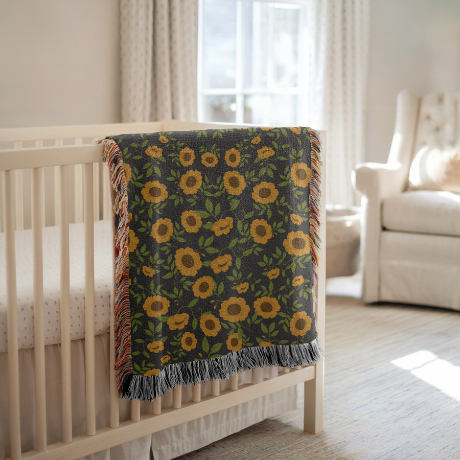 Grey fringed woven blanket covered in an even pattern of ochre sunflowers with bright green leaves and curling vines running between them across the whole face of the cloth.