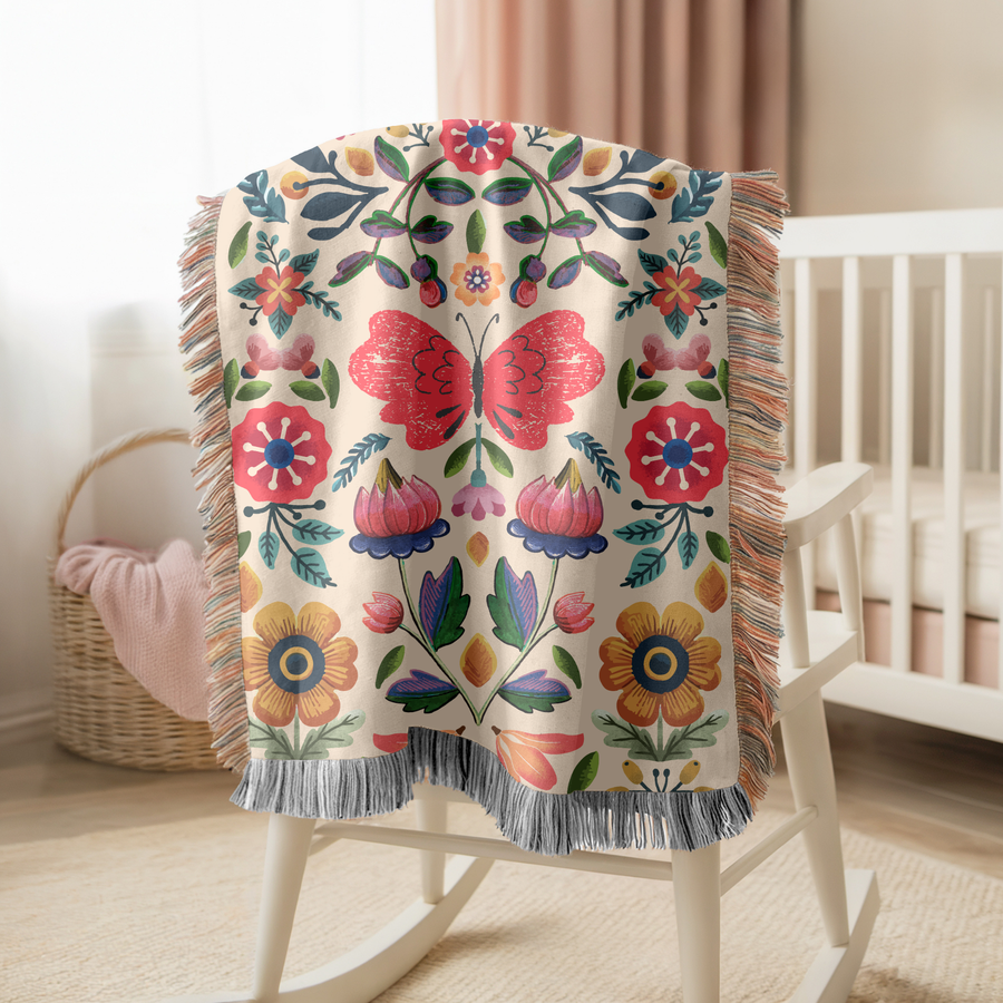 Cream fringed woven blanket printed with a symmetrical folk-art design centred on a large pink butterfly, with red and yellow flowers, blue leaves and tulips mirrored around it.