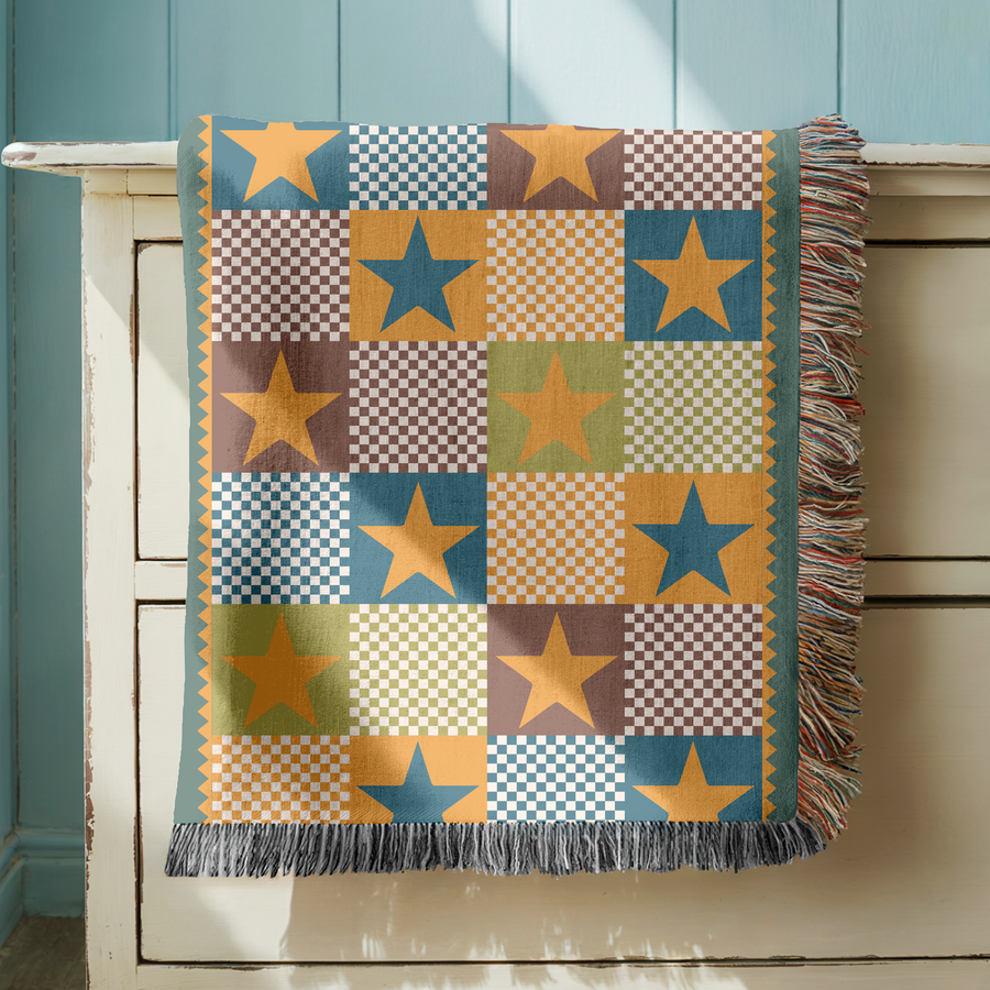 Fringed woven blanket pieced from checkerboard squares in teal, ochre, brown and sage, each square carrying a single large five-pointed star, set inside a gold zigzag border.