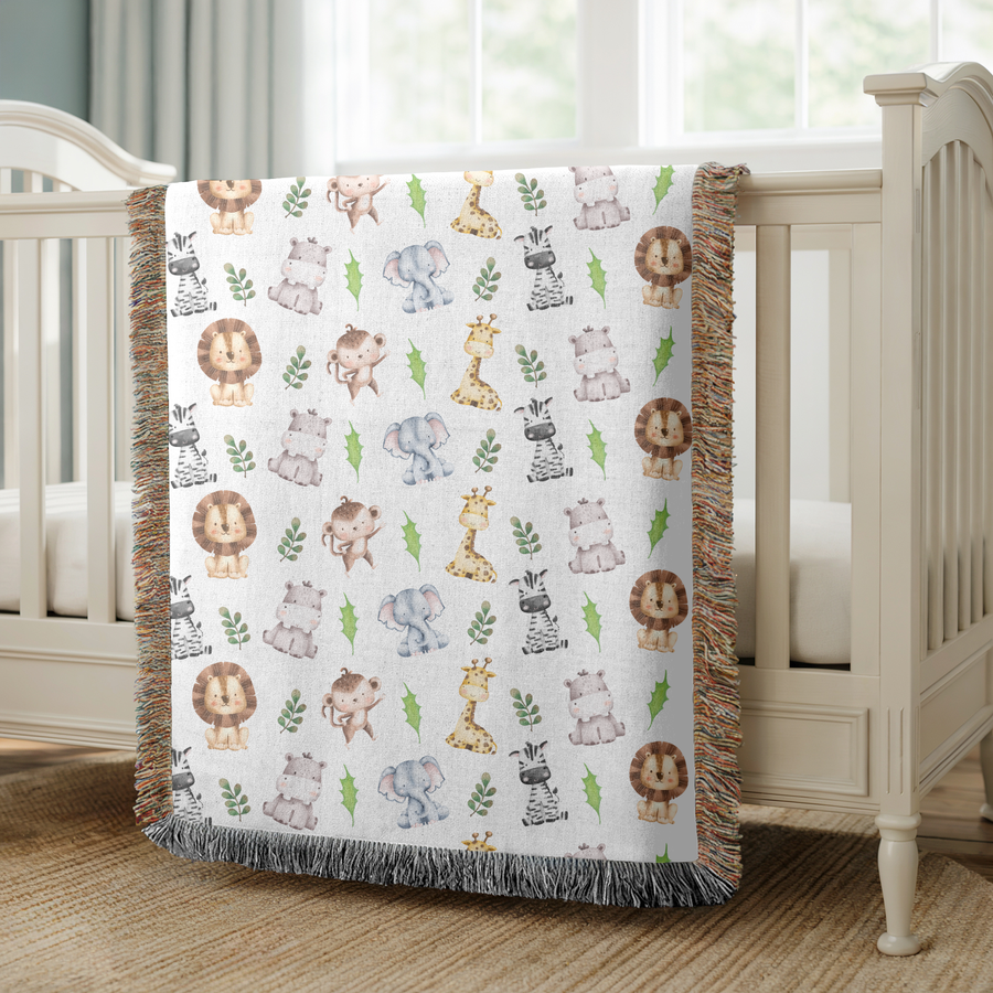 White fringed woven blanket printed with watercolour safari animals, lions, elephants, giraffes, zebras, hippos and monkeys, each drawn in soft washes among small green leaves.