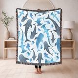 Pale blue fringed woven blanket printed with watercolour sharks, whale sharks, hammerheads and smaller fish, some spotted and some plain, drifting across a washed background.