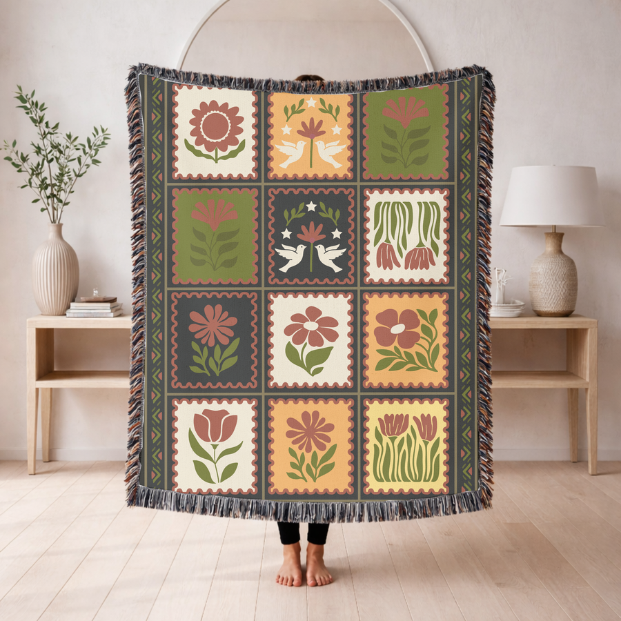 Fringed woven blanket laid out as twelve postage stamps, each holding a folk-art flower or a pair of doves in olive, ochre, cream and terracotta, inside a patterned border.