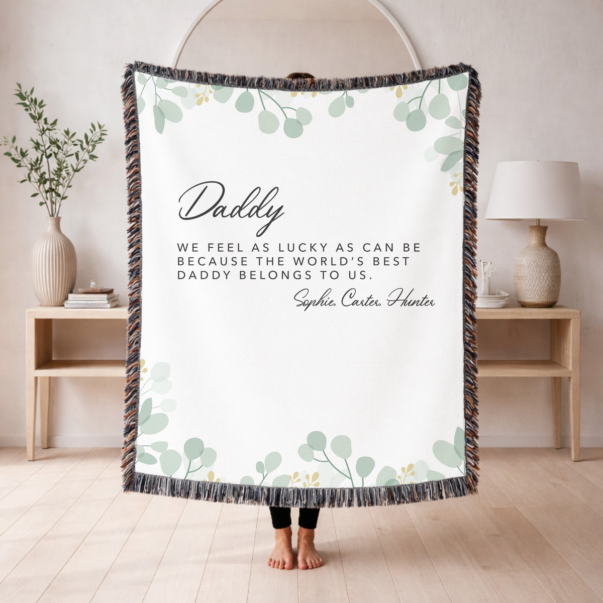 White fringed woven blanket edged with sage eucalyptus, reading Daddy above the line we feel as lucky as can be because the world's best daddy belongs to us, then three names.