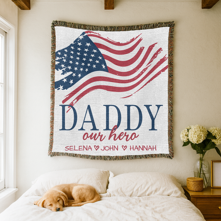 White fringed woven blanket printed with a brushstroke American flag above the word Daddy in navy and our hero in red script, over the names Selena, John and Hannah in red.