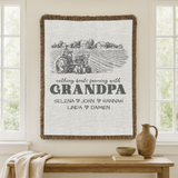 Cream fringed woven blanket with an engraved farm scene of a tractor and farmhouses, reading nothing beats farming with Grandpa above five names divided by small dark hearts.