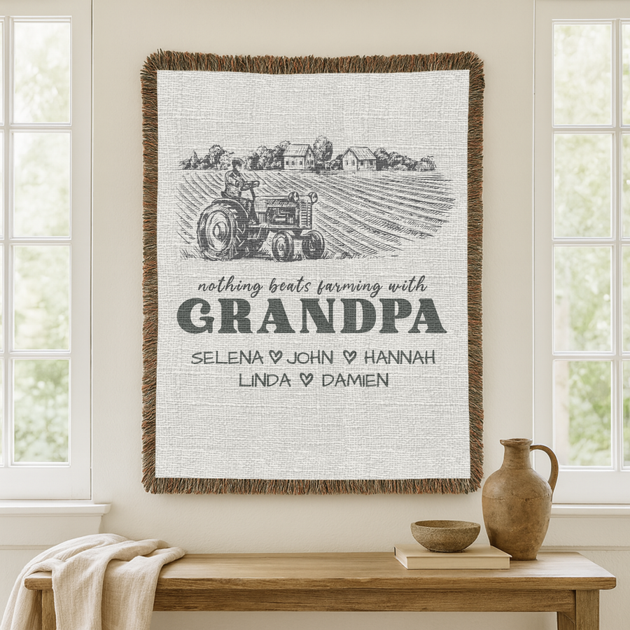 Cream fringed woven blanket with an engraved farm scene of a tractor and farmhouses, reading nothing beats farming with Grandpa above five names divided by small dark hearts.