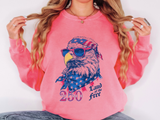 A pink crewneck sweatshirt printed with a bald eagle in star-spangled sunglasses and a flag bandana above 250 and Land of the Free.