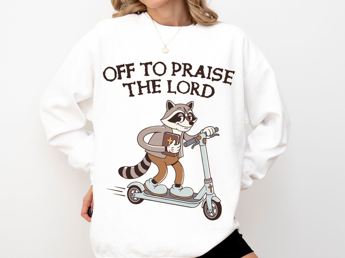 A white crewneck sweatshirt printed with a raccoon in a vest riding a scooter under the words Off to Praise the Lord.