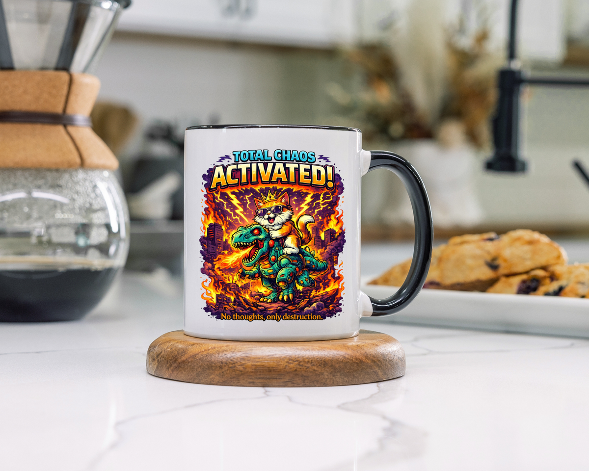 White mug with a black handle and rim, printed with a cartoon cat in a gold crown and sunglasses riding a green robot dinosaur through a burning city, headed Total Chaos Activated.