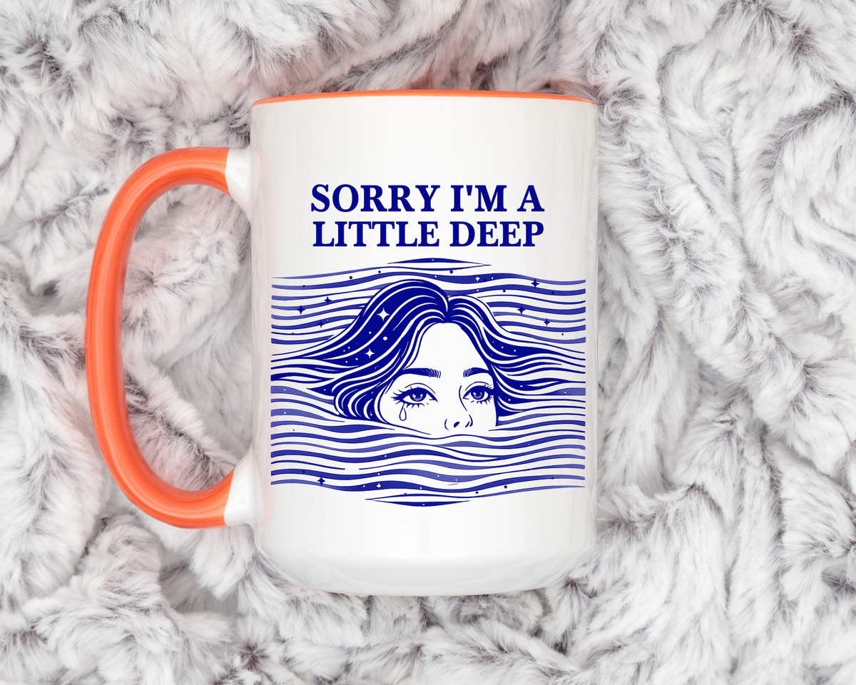 White mug with an orange handle and rim, printed in navy with the words Sorry I'm a Little Deep above a woman's face breaking the surface of stylised waves, her hair streaming out.