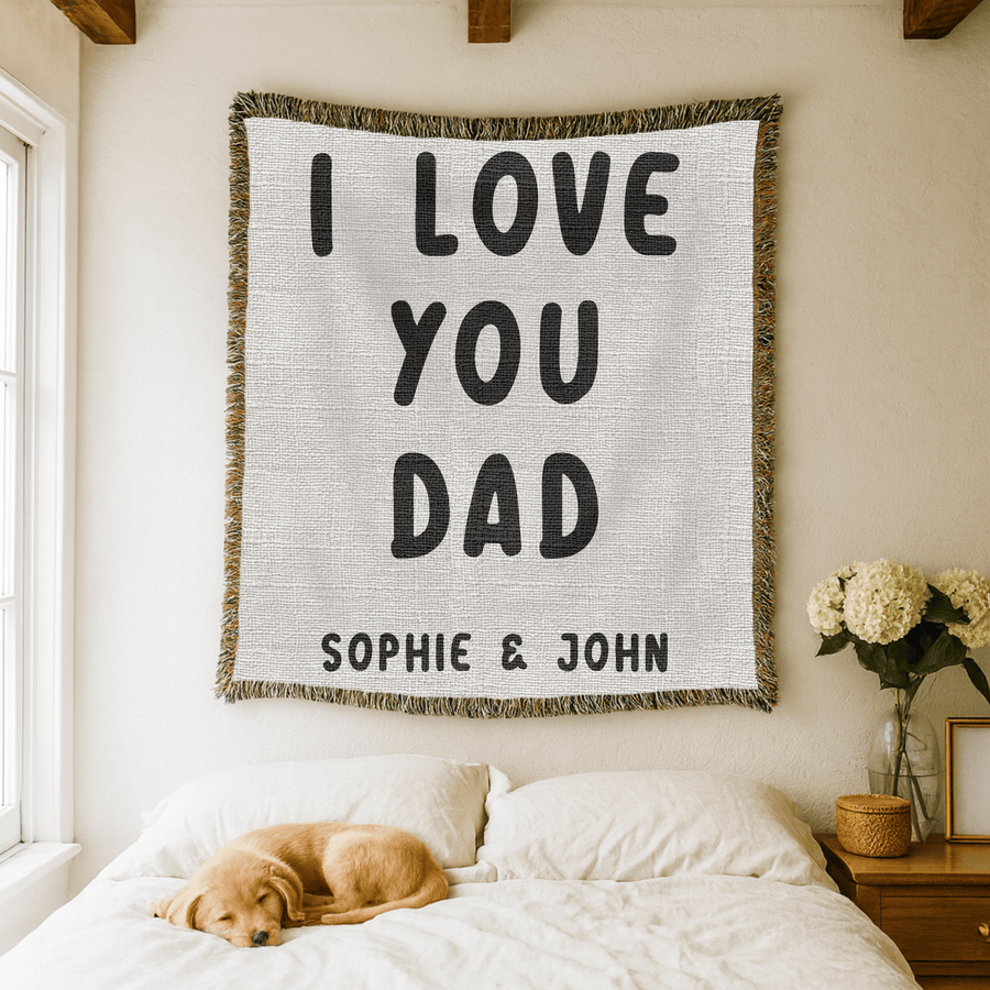 White fringed woven blanket printed with the words I Love You Dad in tall bold black capitals across three lines, with the names Sophie and John set in a row beneath them.