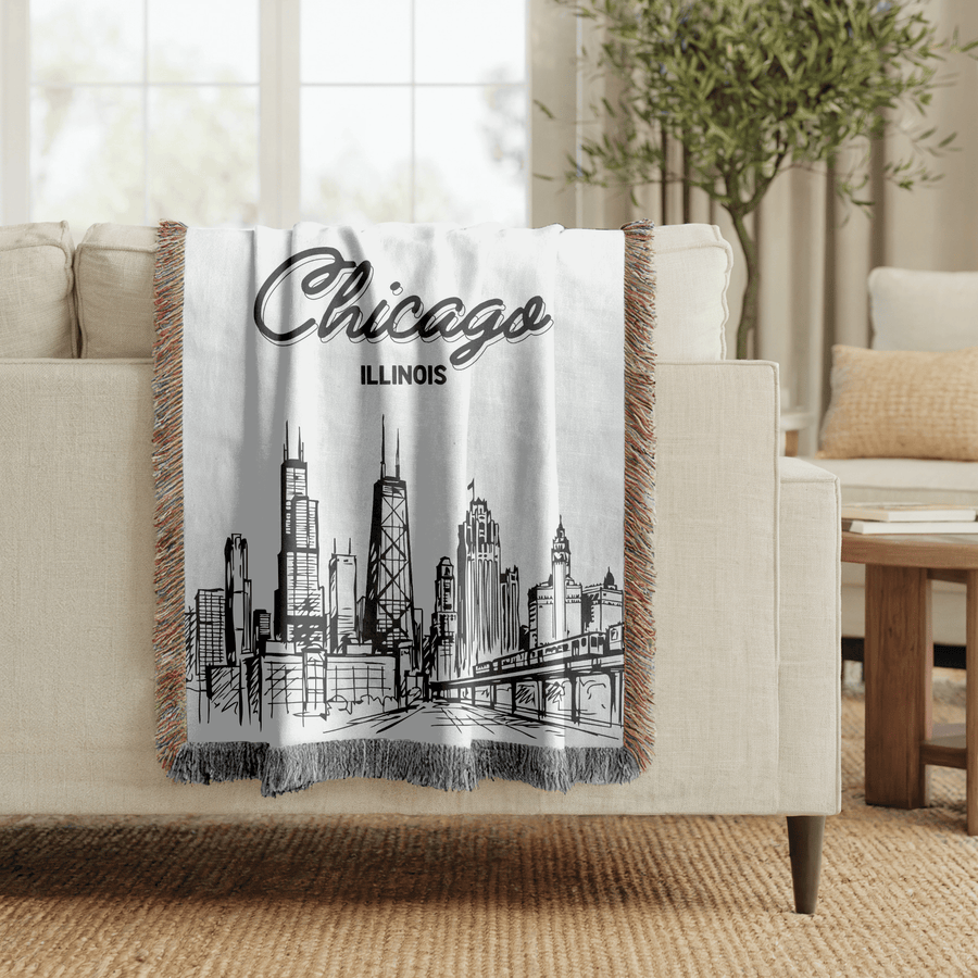 Grey fringed woven blanket reading Chicago in bold script above the word Illinois, over a fine line drawing of the city skyline and its elevated railway along the bottom.