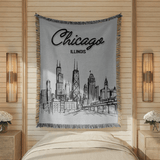 Grey fringed woven blanket reading Chicago in bold script above the word Illinois, over a fine line drawing of the city skyline and its elevated railway along the bottom.