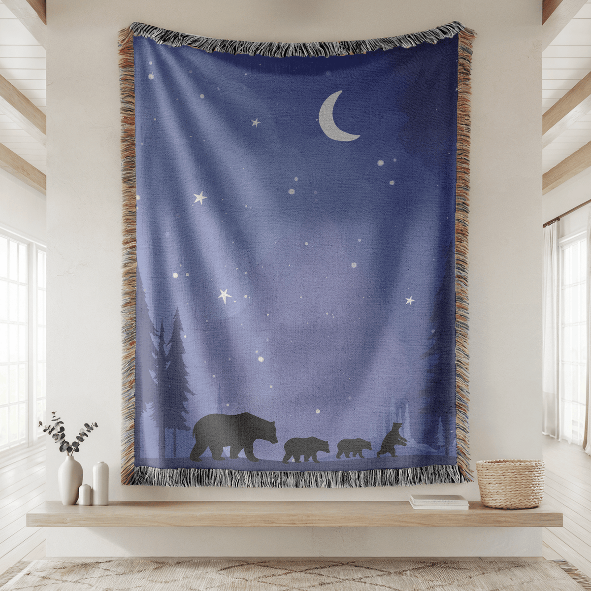 Deep blue fringed woven blanket printed with a crescent moon and stars over a pine treeline, with a mother bear and three cubs walking in silhouette along the lower edge.