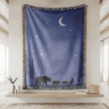 Deep blue fringed woven blanket printed with a crescent moon and stars over a pine treeline, with a mother bear and three cubs walking in silhouette along the lower edge.