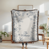 Cream fringed woven blanket printed with a blue line-drawn border of sunflowers and trailing stems with a small bird perched among them, reading The Williams in blue script.
