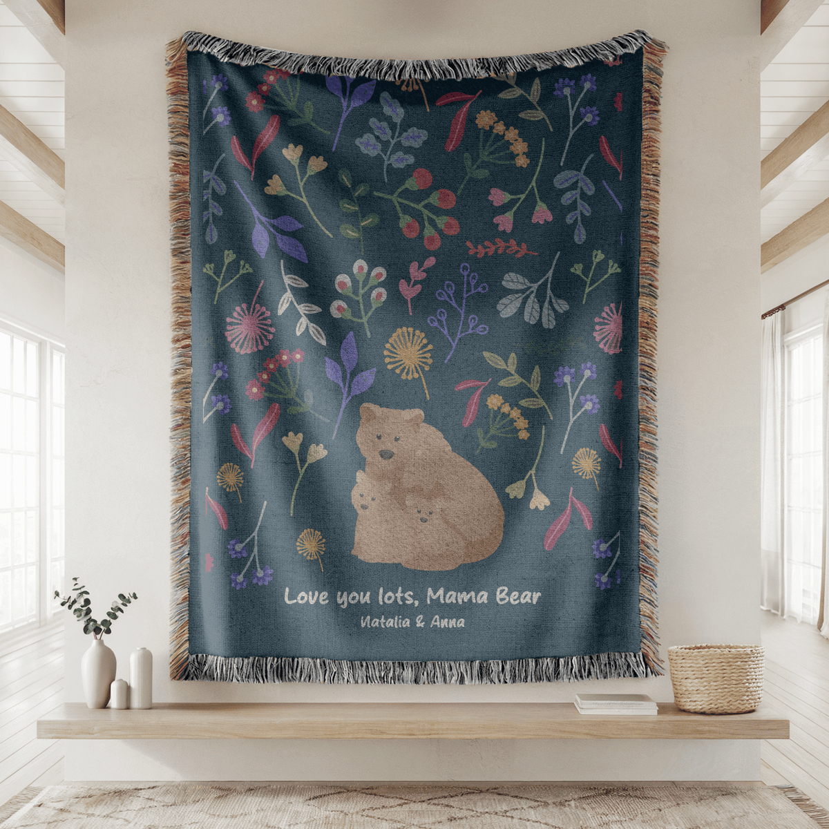 Dark teal fringed woven blanket printed with folk-art flowers above a tan mother bear and her two cubs, reading Love you lots, Mama Bear and the names Natalia and Anna below.
