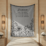 Two-tone grey fringed woven blanket reading Grandparents make the world a little bit softer, a little bit kinder, a little bit warmer, above a row of line-drawn wildflowers.