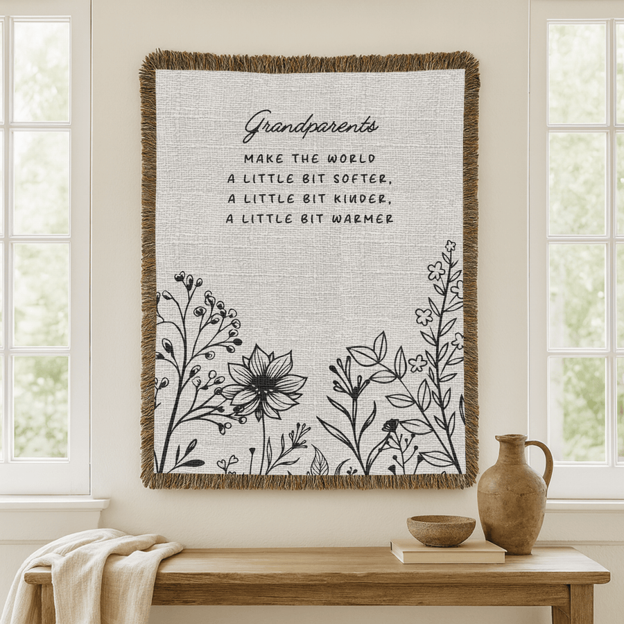 Two-tone grey fringed woven blanket reading Grandparents make the world a little bit softer, a little bit kinder, a little bit warmer, above a row of line-drawn wildflowers.