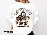 White sweatshirt printed with a grinning bigfoot carrying a large open-mouthed fish under one arm, headed Keepin It Reel in an arc of outlined capitals curving above his head.