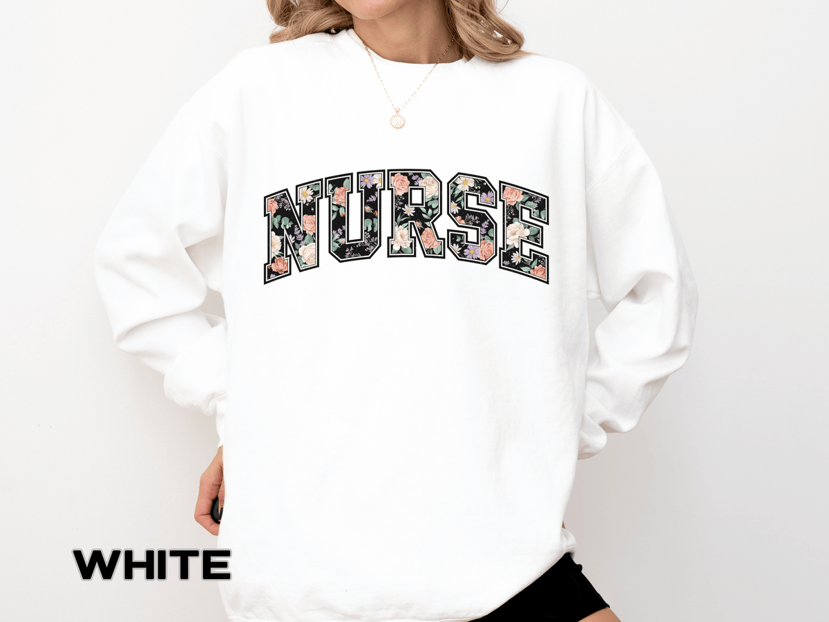 A white crewneck sweatshirt printed with NURSE in varsity letters filled with a dark floral pattern.