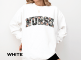 A white crewneck sweatshirt printed with NURSE in varsity letters filled with a dark floral pattern.