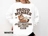 A white crewneck sweatshirt printed with a man napping in a recliner between Proud Member of the and Just Resting My Eyes Club.