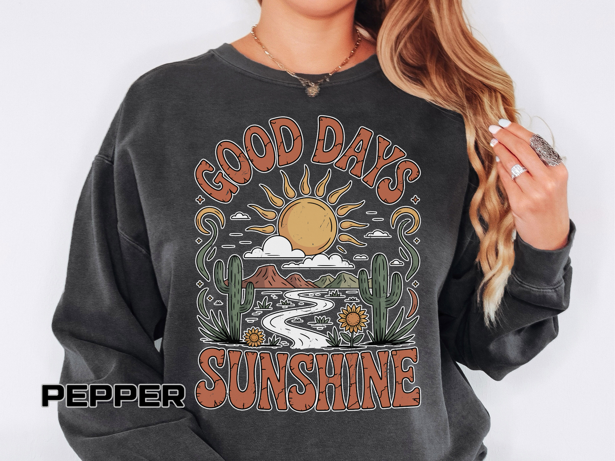 A dark gray crewneck sweatshirt printed with a retro desert scene of a sun, cacti and a winding road framed by the words Good Days Sunshine.