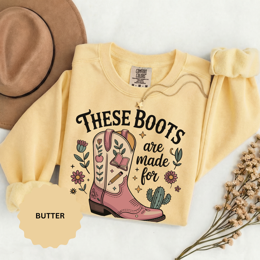 Chambray sweatshirt printed with a pink and cream cowboy boot decorated with a book, a pencil and an apple among flowers and a small cactus, headed These Boots Are Made For Teaching.