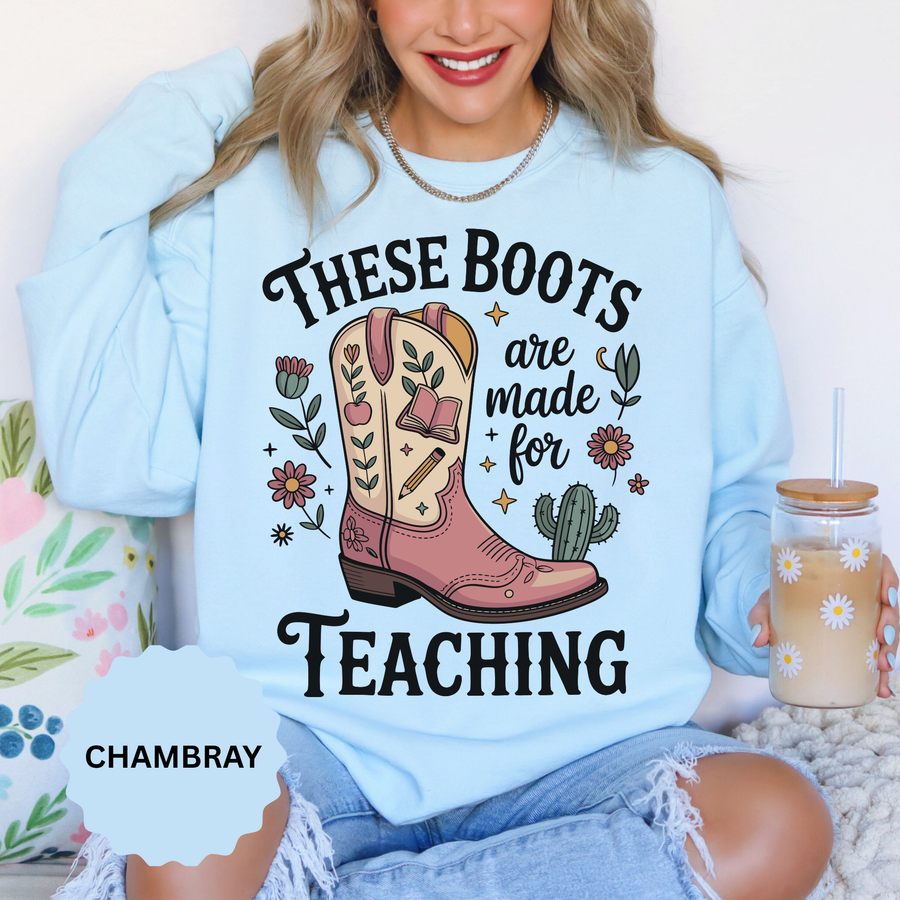 Chambray sweatshirt printed with a pink and cream cowboy boot decorated with a book, a pencil and an apple among flowers and a small cactus, headed These Boots Are Made For Teaching.