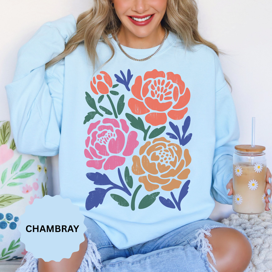Chambray sweatshirt printed with four bold block-print roses in coral, pink and ochre, each bloom filled with fine line detail and framed by navy and dark green leaves and stems.