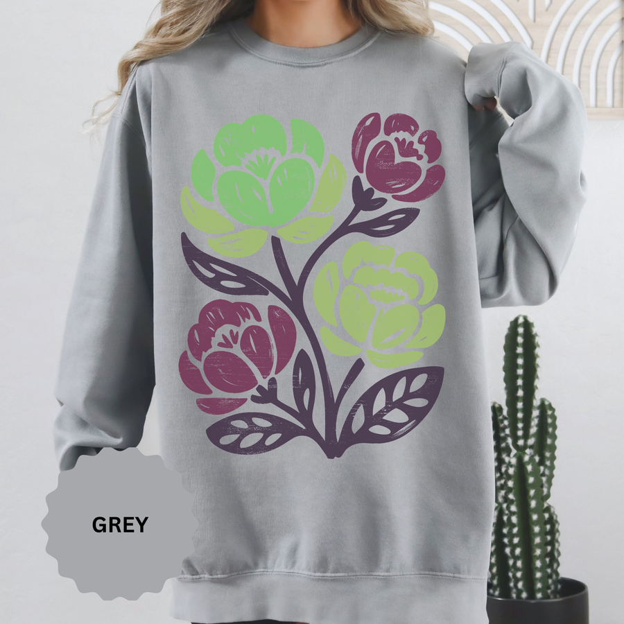 Grey sweatshirt printed with block-print flowers in lime green and deep magenta on dark purple stems, the leaves outlined in the same purple with the rough texture of a hand-cut lino print.