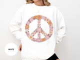 White sweatshirt printed with a large peace sign built entirely from retro daisies and blooms in dusty pink, apricot and cream, with curling leaves filling the centre of the ring.