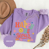 A purple crewneck sweatshirt printed with Happy to See Your Face in retro rainbow lettering with a smiley face and stars.